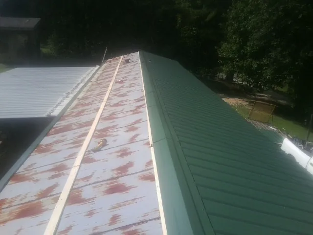 Old rusted panels beside newly installed green metal roofing — Wind Damage Roof Repair by Roofing Brothers in Riverside