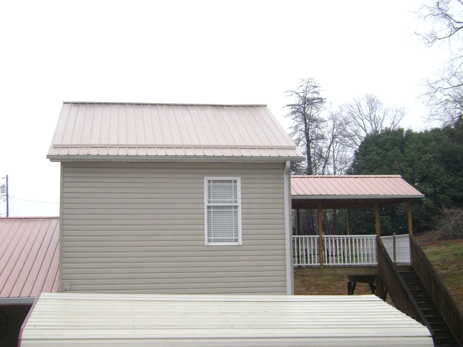 Tan metal roofs on a two story addition and attached porch, from a Roof Replacement job in Riverside